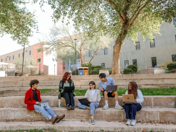 A group of five people sit and laugh together under trees.
